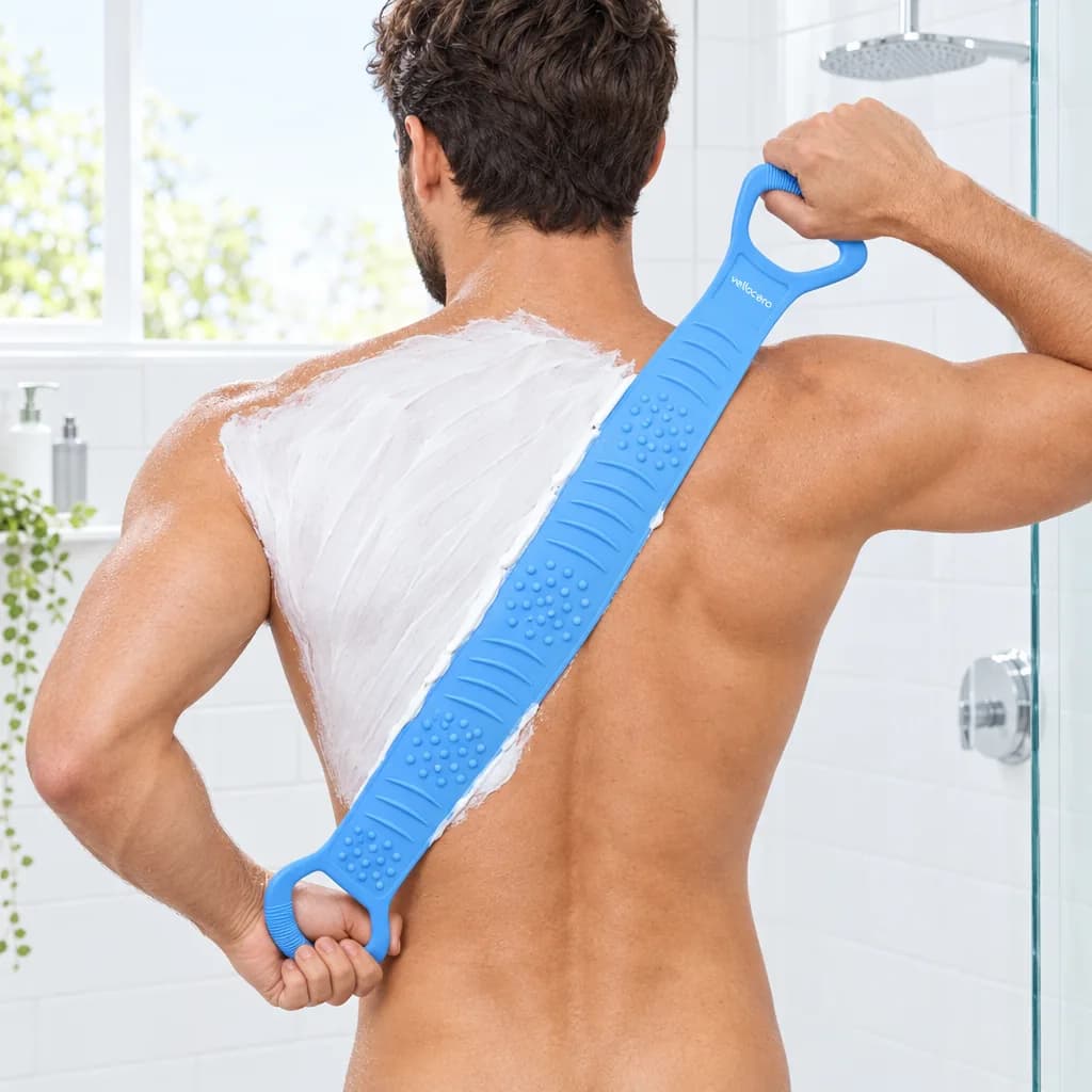 Hombre de espaldas en la ducha extendiendo crema depilatoria blanca por la espalda con el cepillo Vellocero azul sujeto por las dos asas