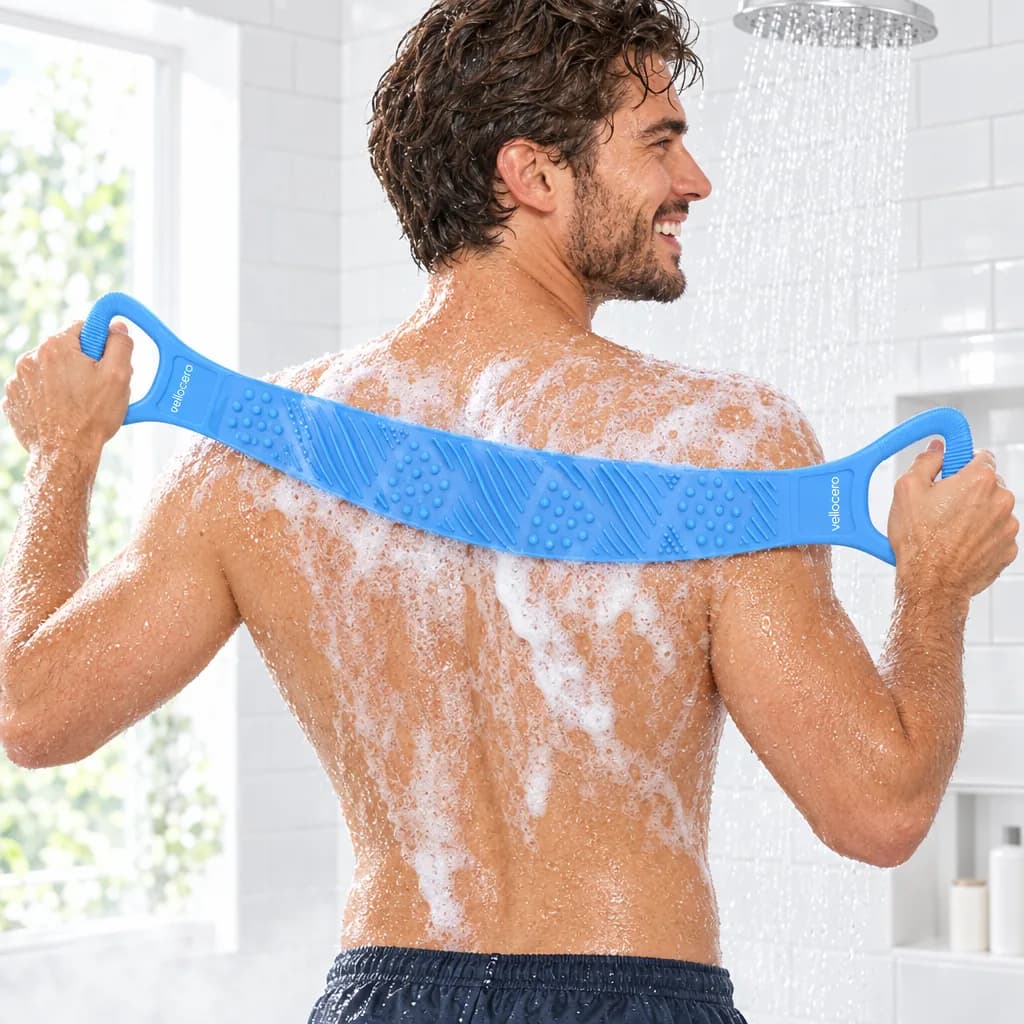 Hombre sonriente en la ducha frotándose la espalda con espuma, sujetando el cepillo Vellocero azul por las dos asas